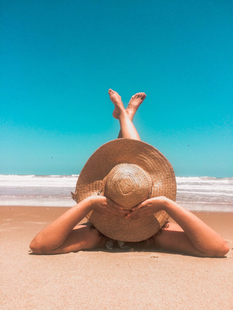 een vrouw die in de zomer op het strand ligt met een grote hoed en haar benen in de lucht